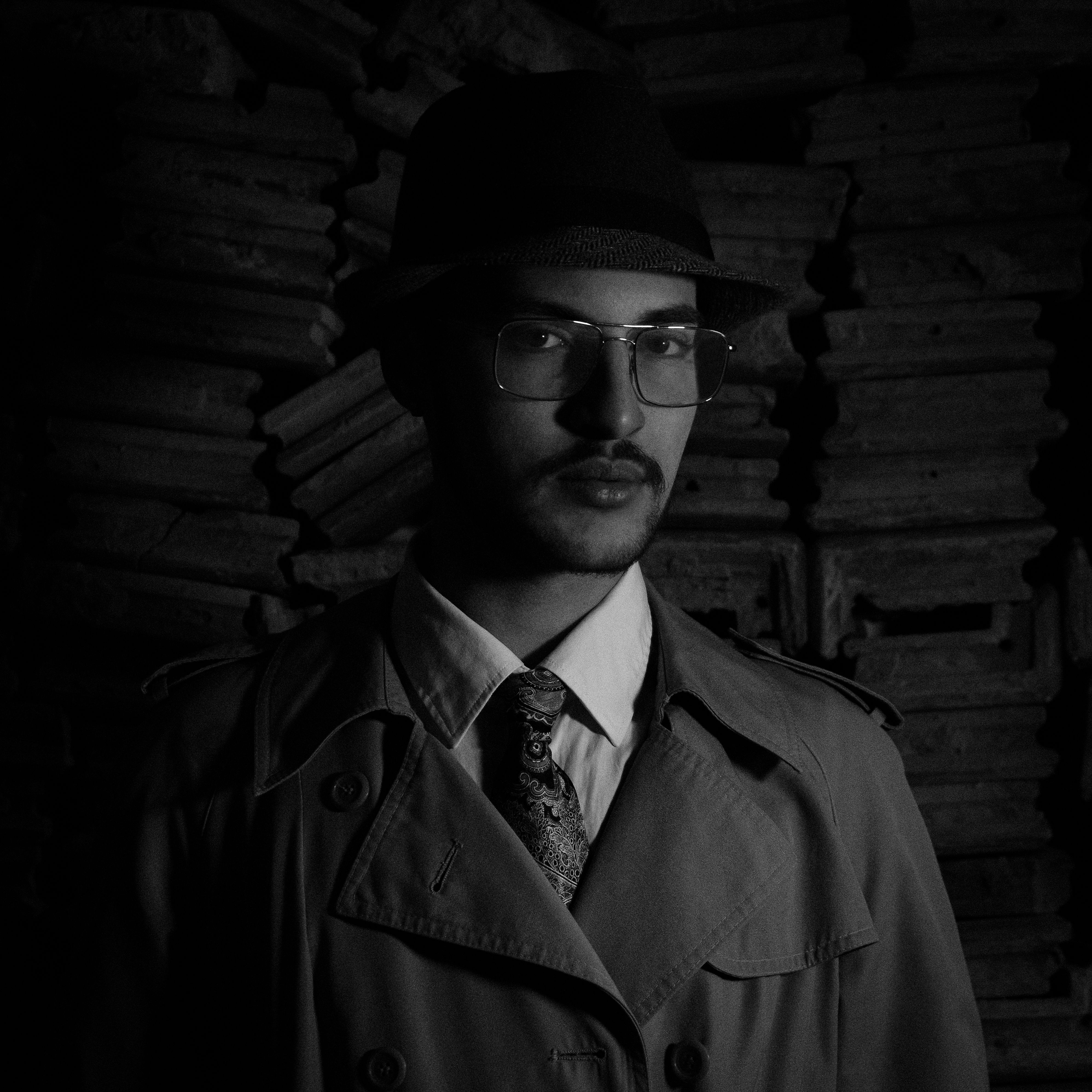 Elegant black and white portrait of a man in a trench coat and hat, exuding mystery and style.