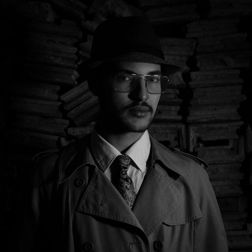 Free Elegant black and white portrait of a man in a trench coat and hat, exuding mystery and style. Stock Photo