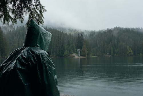 A Person in a Raincoat Sitting on the Lakeshore 