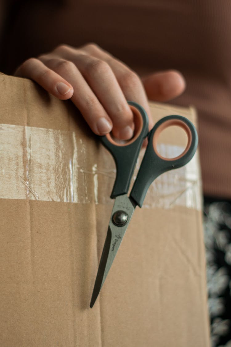 Holding Small Sharp Scissors And A Cardboard Box