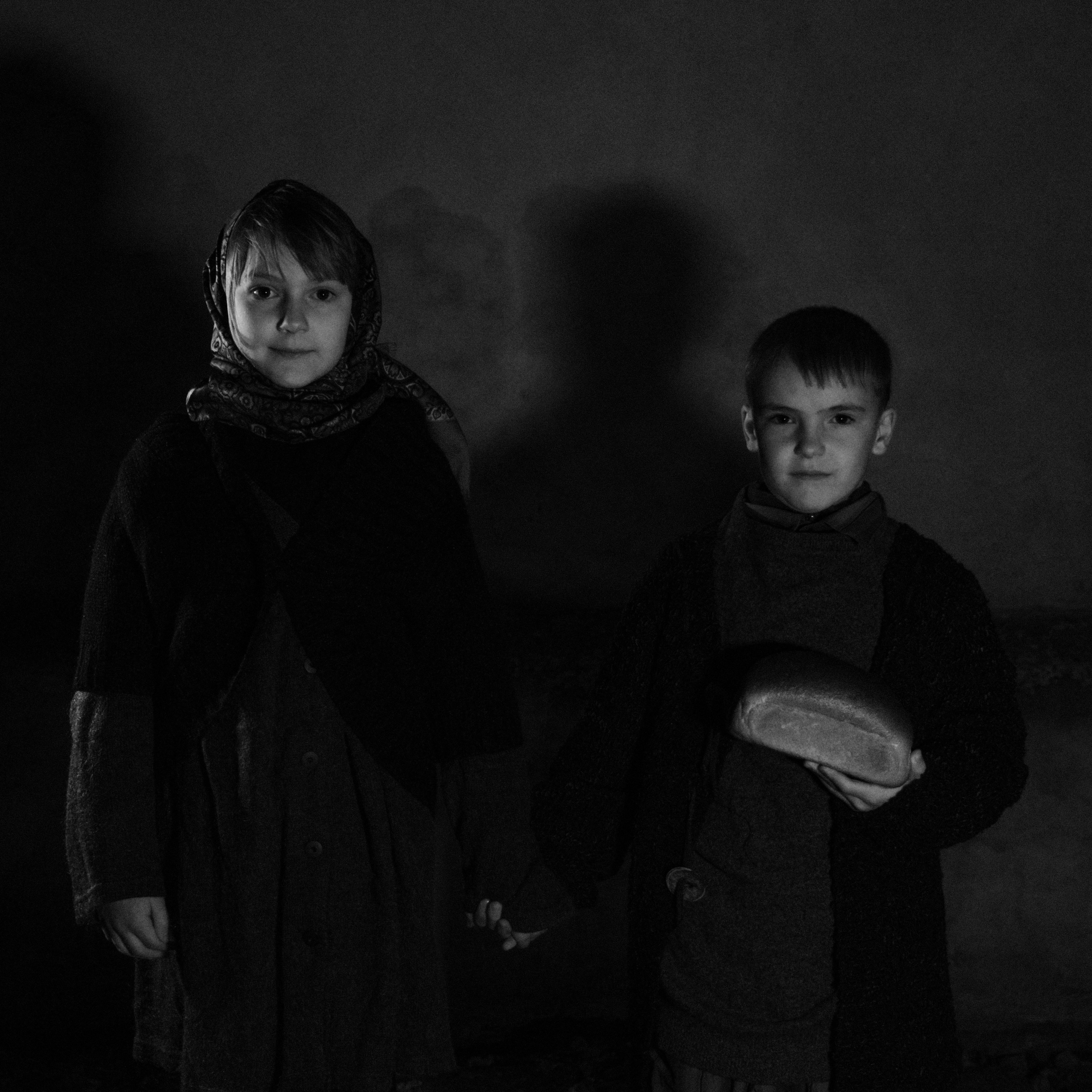 Two children holding hands and bread in a vintage, moody black and white scene.
