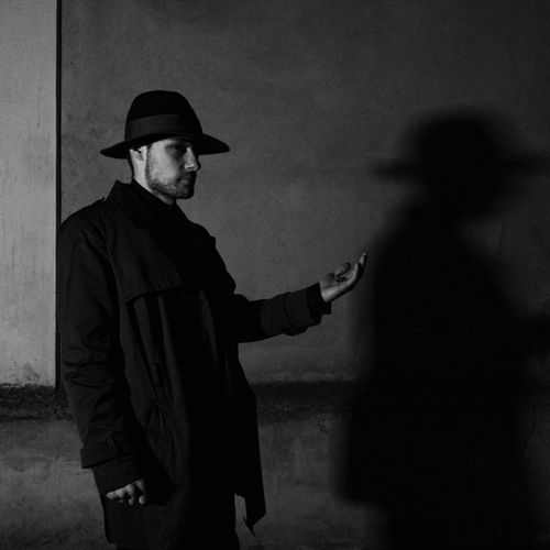Free A dramatic black and white portrait of a man in a hat casting a shadow on the wall. Stock Photo