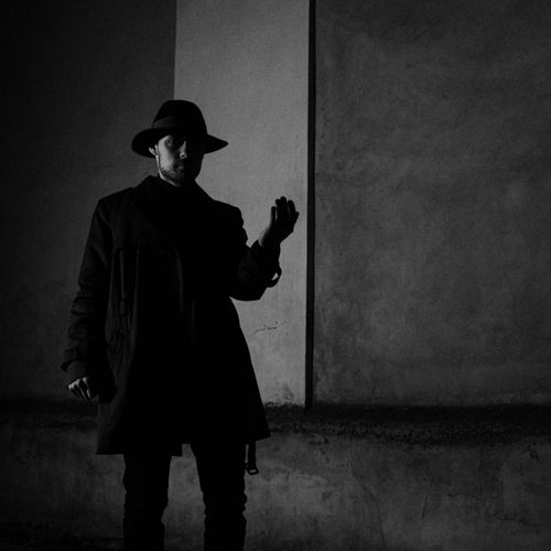 Free Cinematic black and white portrait of a man in shadow, wearing a hat and trench coat, evoking mystery. Stock Photo