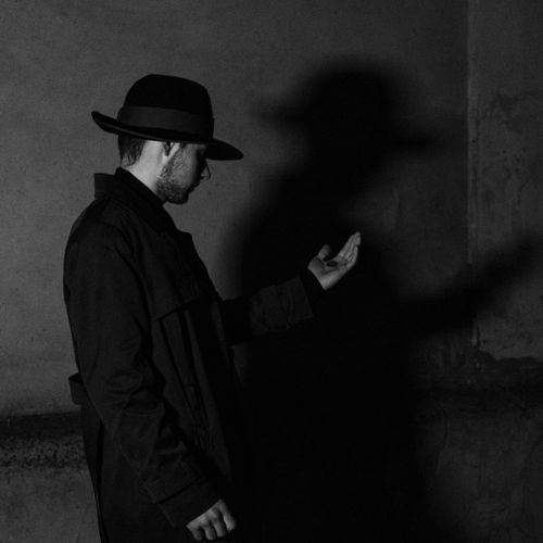 Free Elegant black and white portrait of a man in a hat casting a dramatic shadow, in a studio setting. Stock Photo