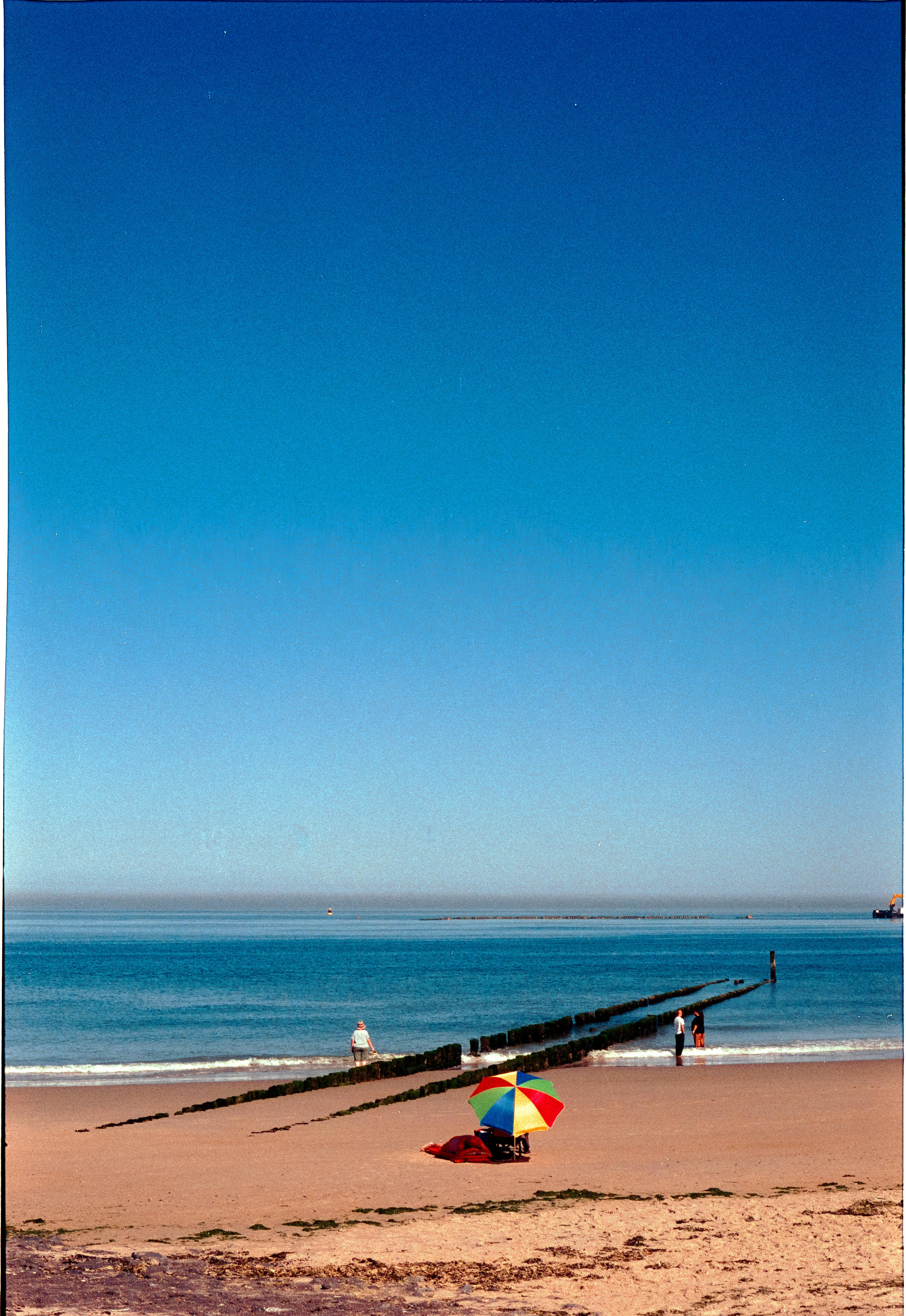 Relaxing beach scene with a rainbow umbrella under clear blue skies.