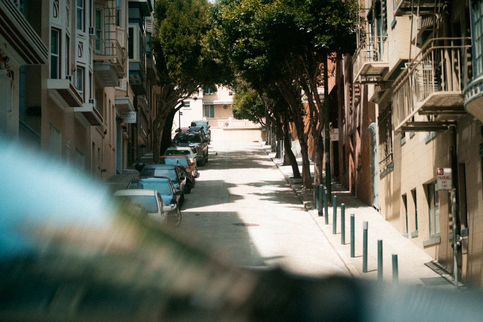 A sunlit uphill street in San Francisco's residential area with parked cars and trees.