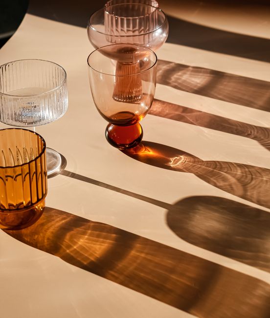Glass cups casting long shadows on a sunlit table. Modern minimalist aesthetic.