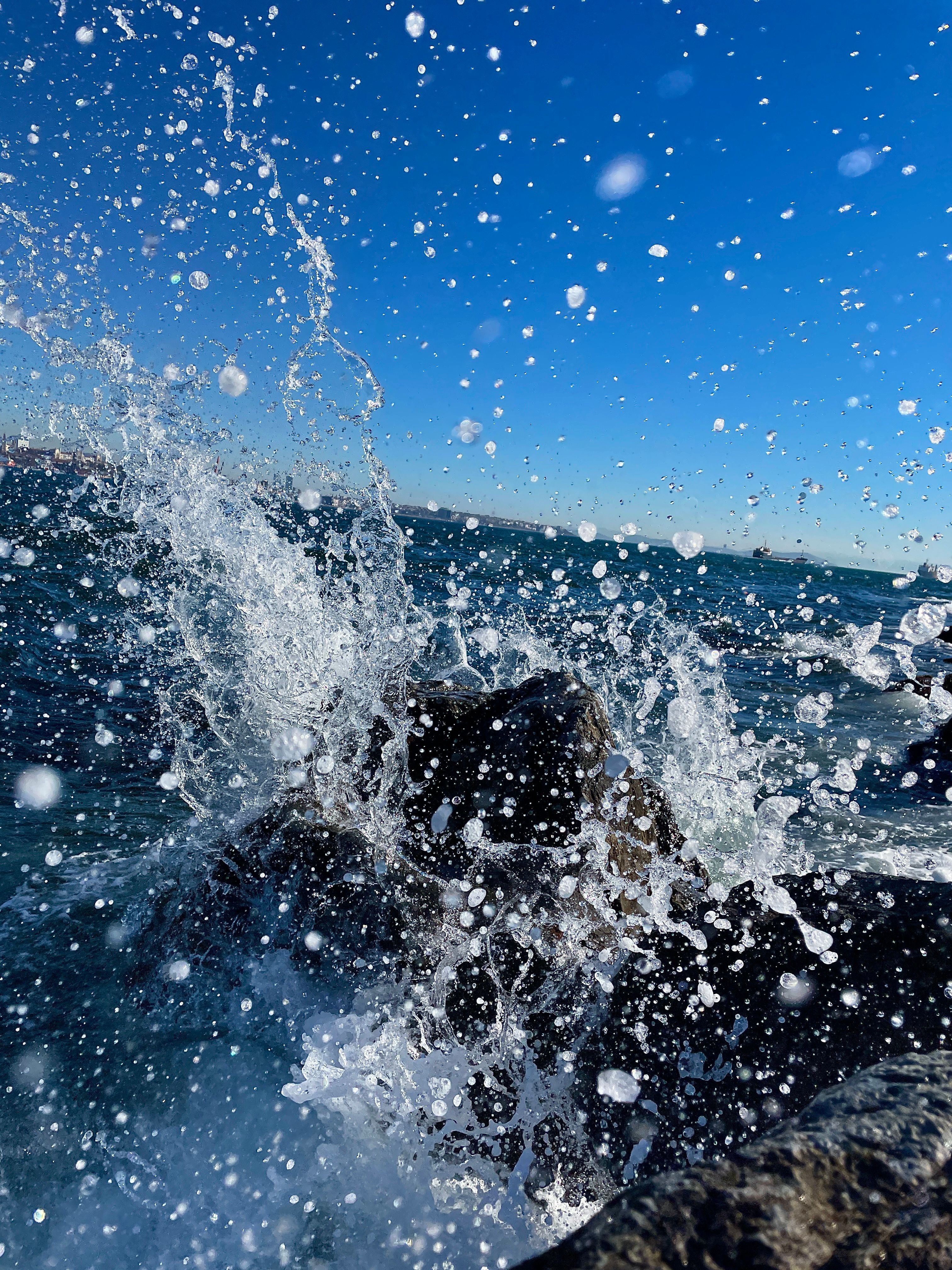 Fotomural Una captura dinámica de las olas del océano salpicando contra las rocas bajo un cielo azul claro.