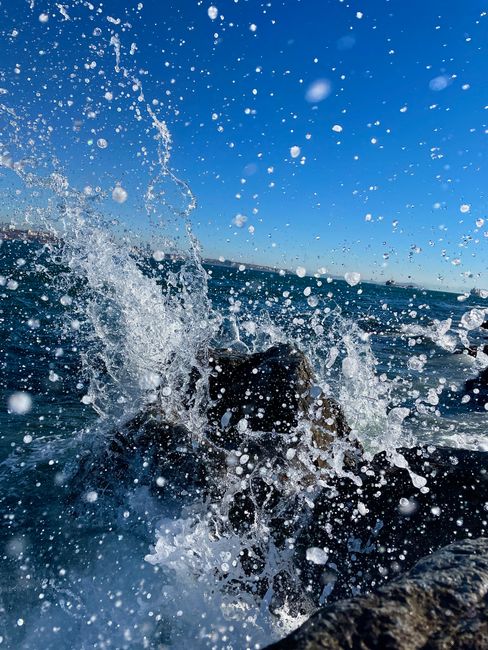 Fotomural Una captura dinámica de las olas del océano salpicando contra las rocas bajo un cielo azul claro.