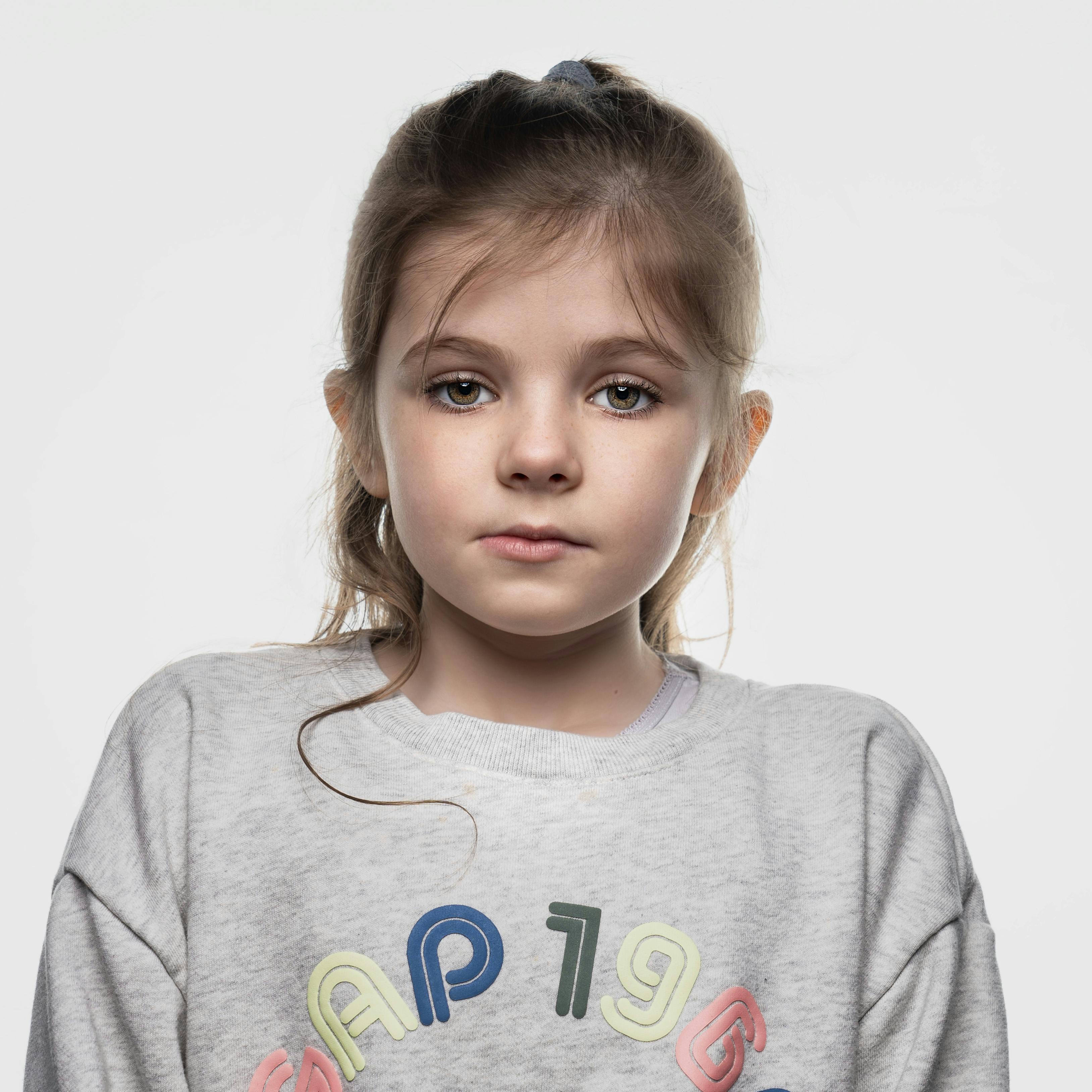 A thoughtful portrait of a young girl in a casual sweatshirt on a white background.