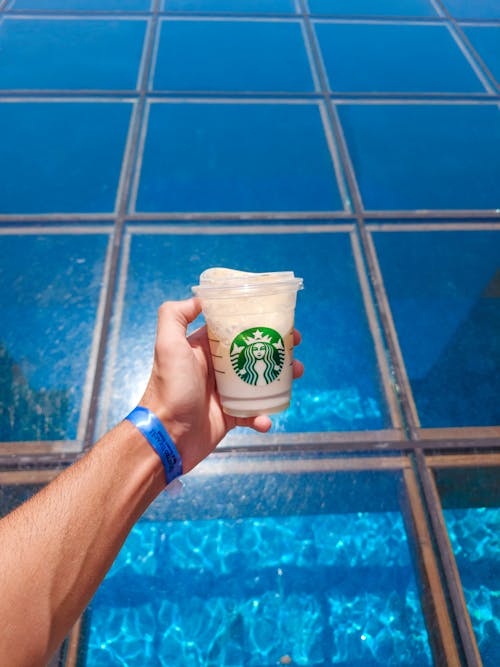 Close-up of a Man Holding a Starbucks Drink on the Background of Glass