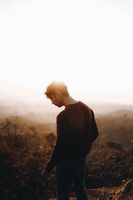 Silhouette of a man standing on a mountain with a foggy background and a warm sunrise.