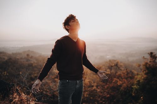 Free A young man standing on a misty hill during sunrise, embracing the light and nature. Stock Photo