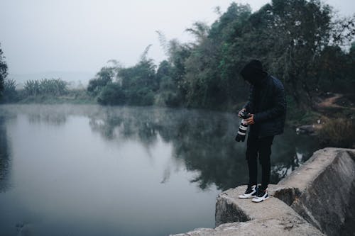 Photographer Standing on Rock near Lake in Fog