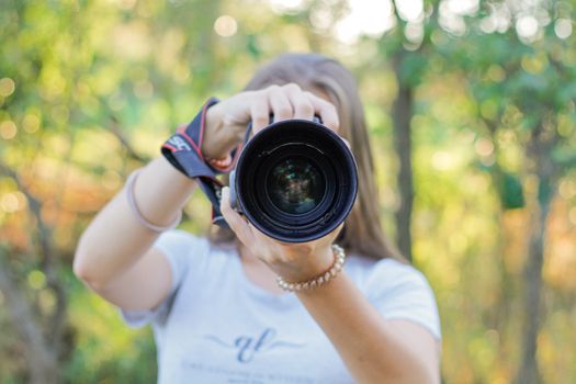 Woman holding a camera lens photographing in a park during fall, embracing the autumn atmosphere.