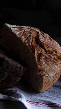 Close-up of rustic sourdough bread loaf sliced on a cloth with dark background.
