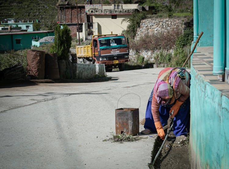 Elderly Woman With Bucket Cleaning Street