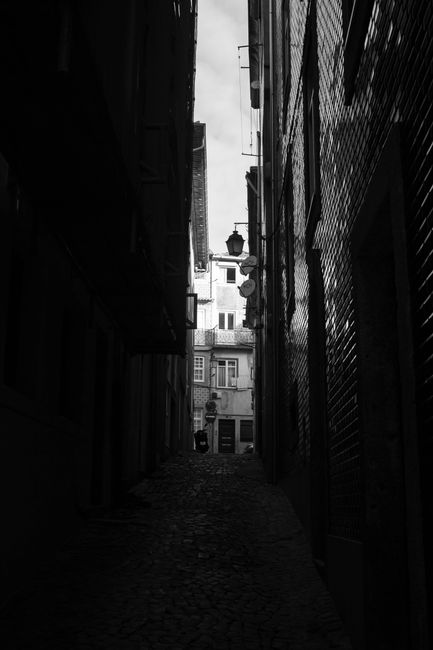 A dark and narrow alley with cobblestone pavement in Porto, Portugal showcases the city's historic charm.