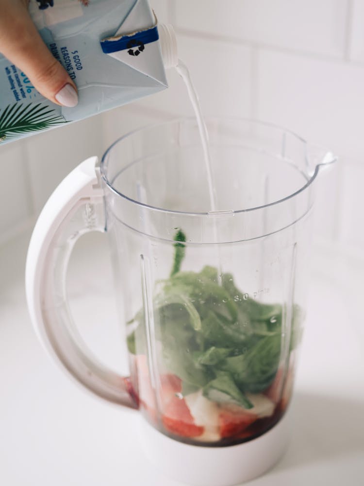 Hand Pouring Milk Into Blender With Fruits And Spinach