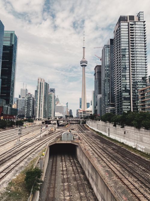 Free Iconic CN Tower amid Toronto's skyline with railway tracks leading into the cityscape. Stock Photo