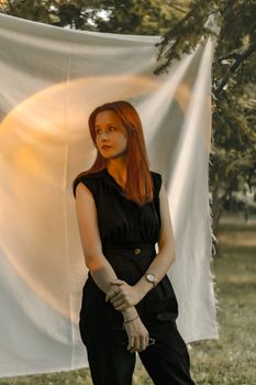 Stylish portrait of a redhead woman in black attire outdoors with artistic backlighting.