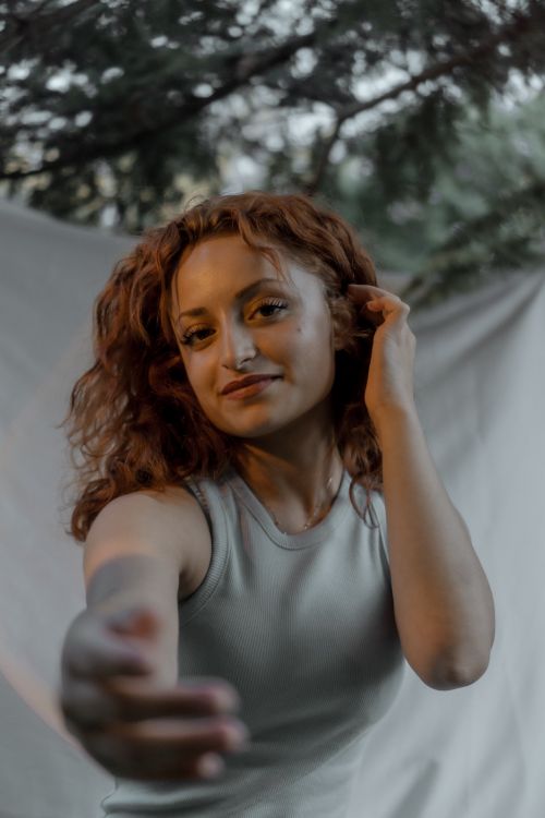 Free Portrait of a young woman with curly hair reaching towards the camera outdoors. Stock Photo
