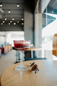 A stylish Clover Club cocktail served in an elegant glass on a wooden table indoors, enhanced by modern lighting.