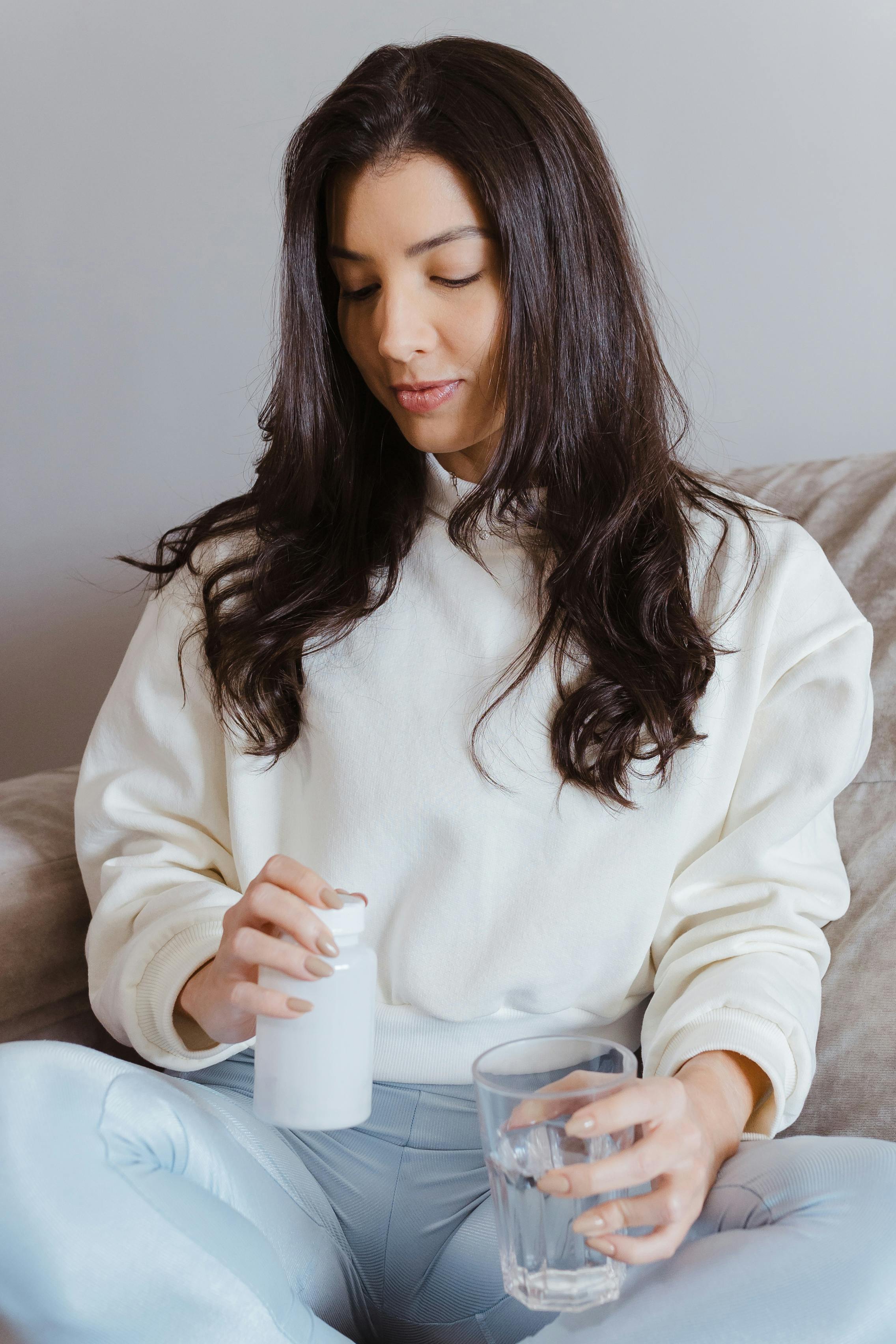 Young woman holding a pill bottle and a glass of water, symbolizing healthcare and wellness indoors.