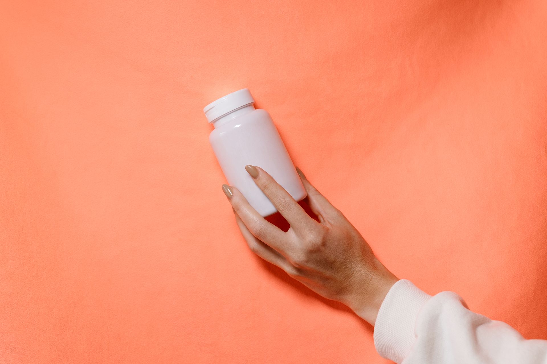 Close-up of a hand holding a white bottle against a vibrant orange backdrop.