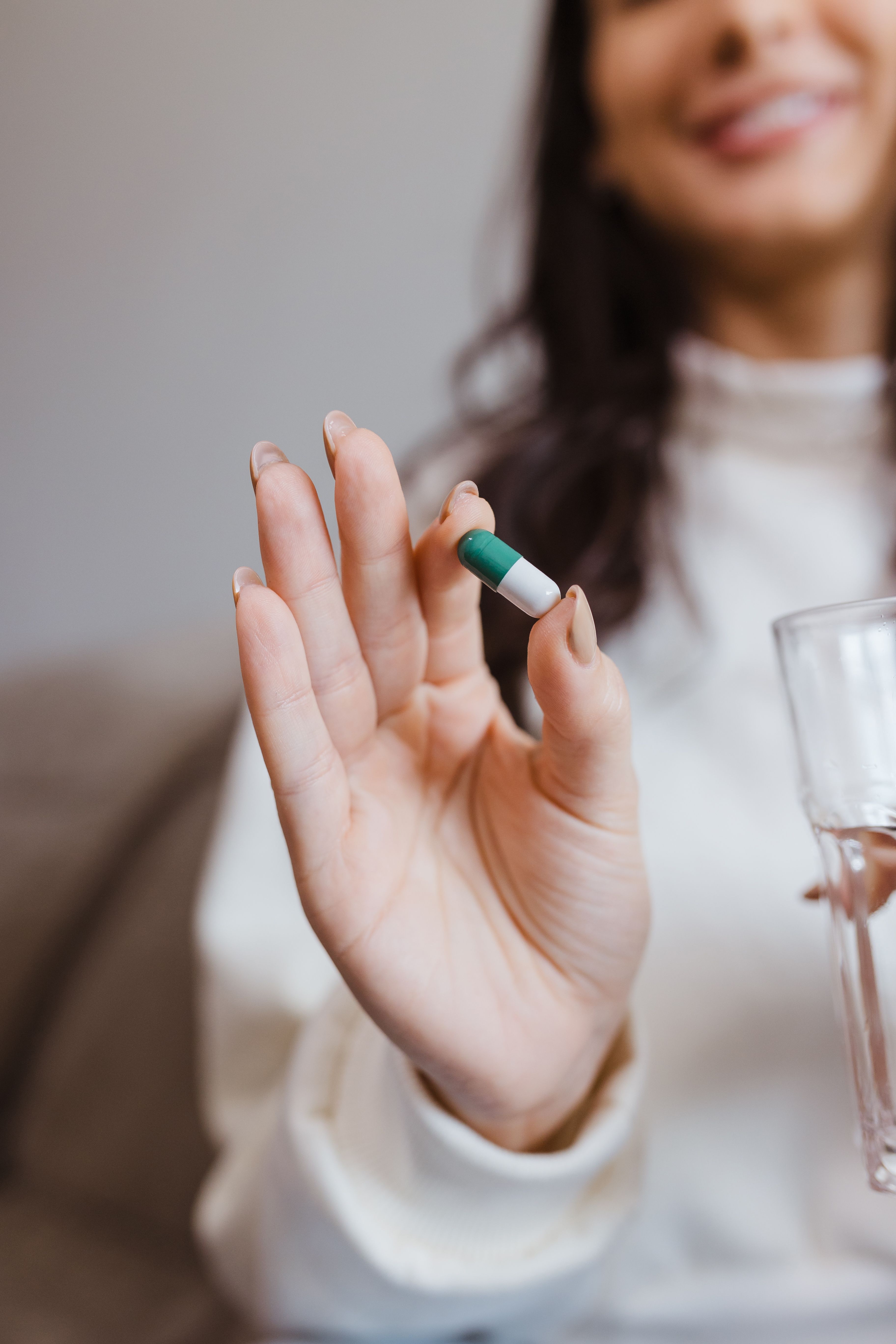 Woman holding a supplement capsule and glass of water
