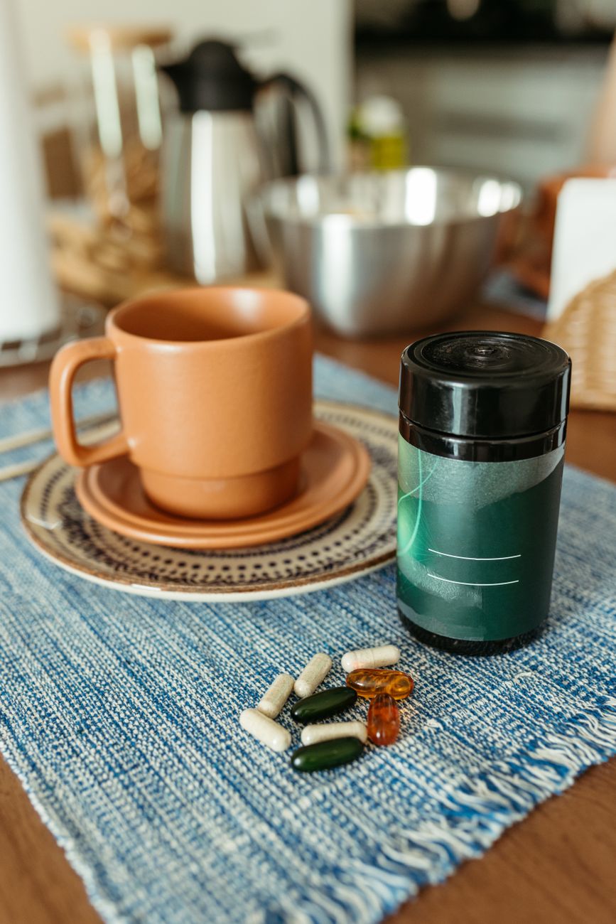 Vitamins and supplements on a kitchen table beside a cup