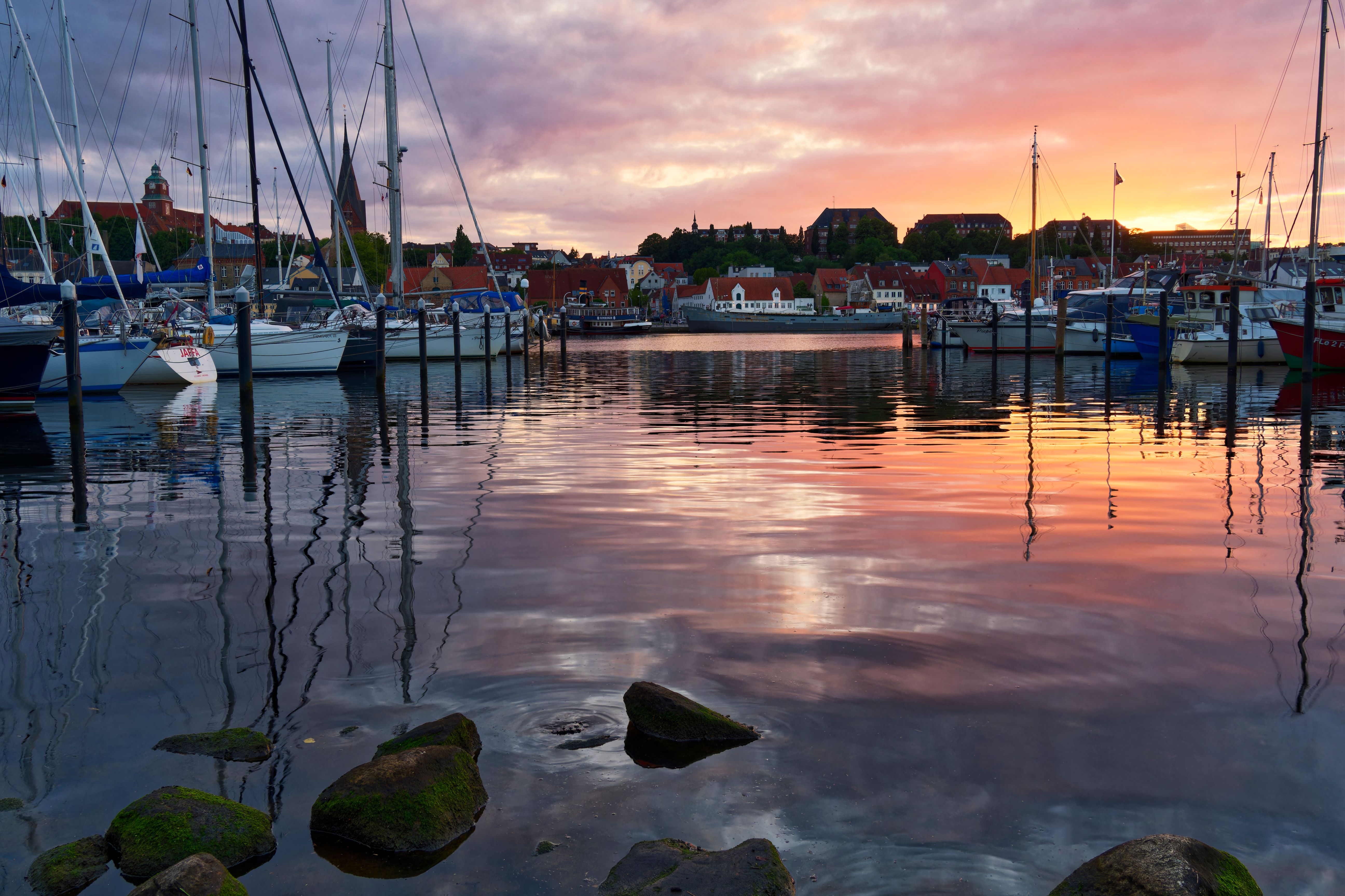 Stunning sunset over Flensburg marina with yachts and reflections in calm waters.