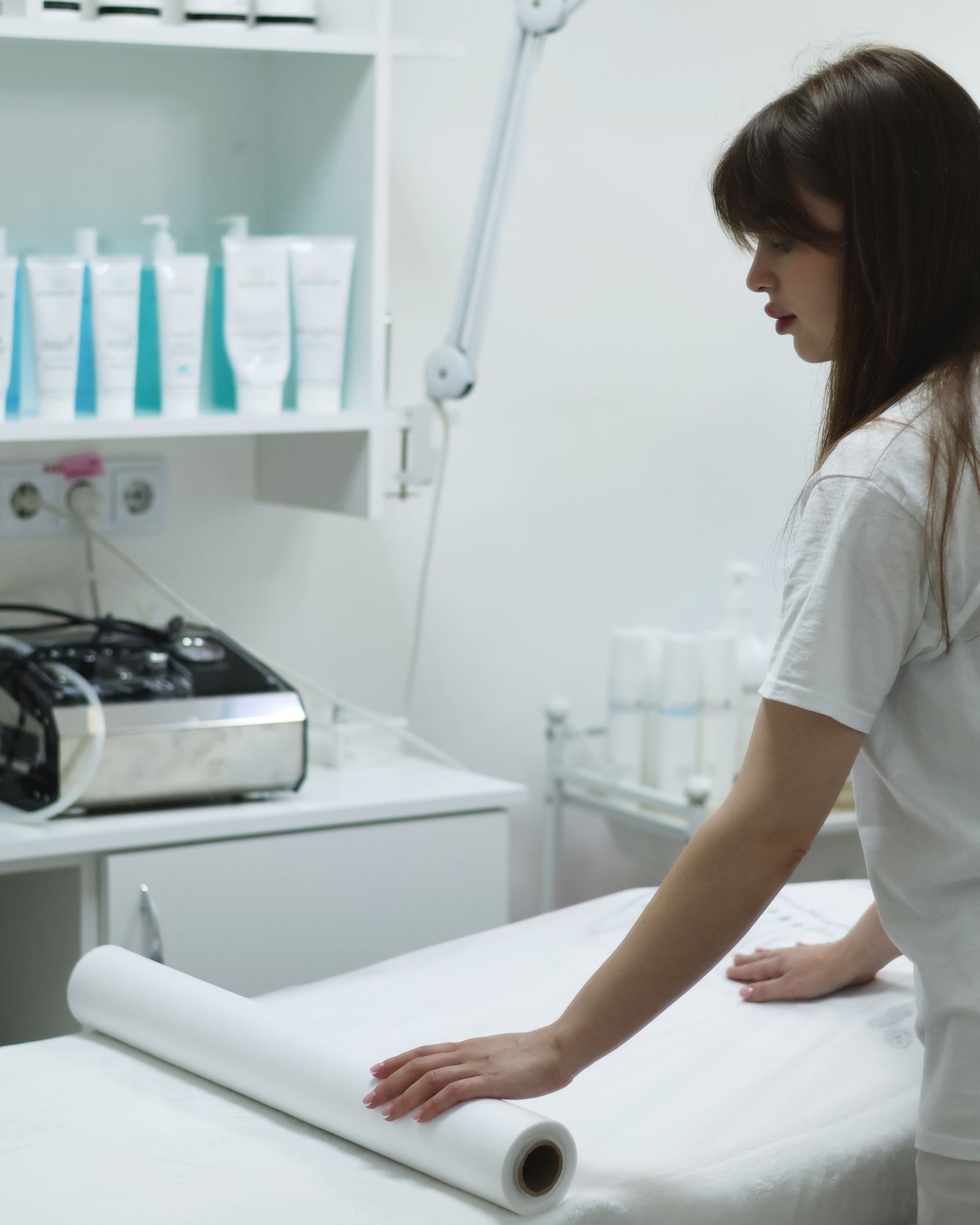 Esthetician in a white uniform preparing a treatment bed