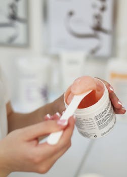 A person scooping a peach-colored skincare gel with a spatula from a container.