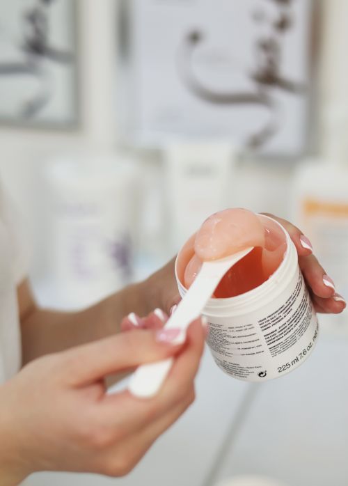 Free A person scooping a peach-colored skincare gel with a spatula from a container. Stock Photo