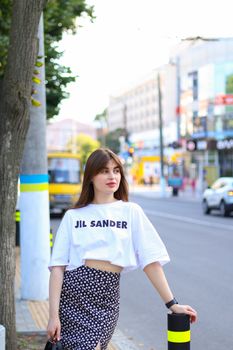 A stylish young woman stands on a city street wearing a Jil Sander blouse and polka dot skirt.
