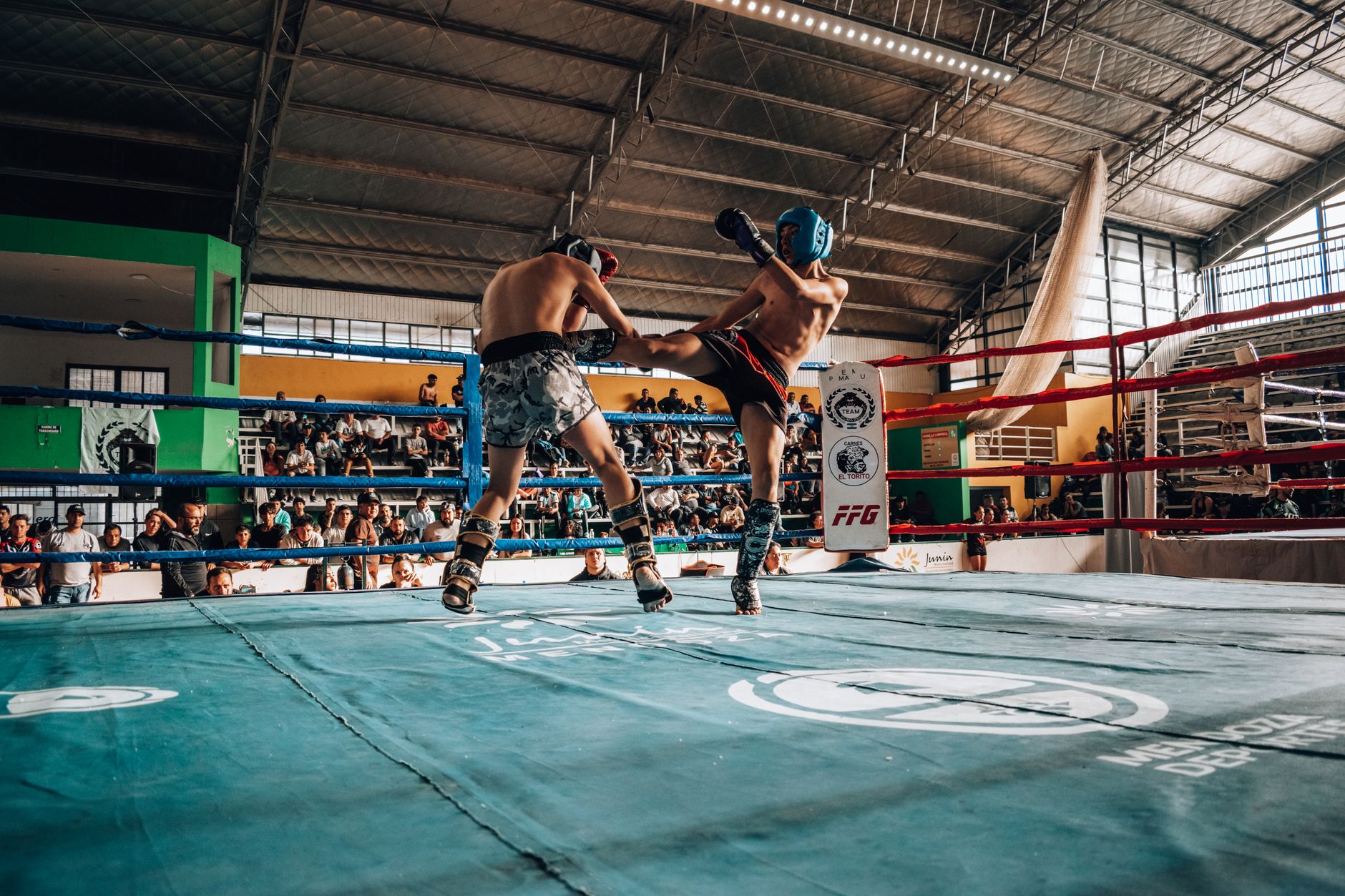 Two athletes engaged in high-energy kickboxing match in a packed indoor arena.