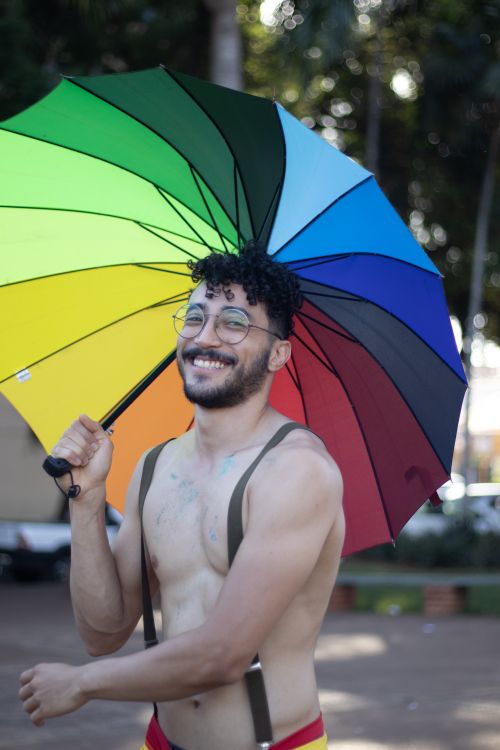 Free Shirtless man with a rainbow umbrella smiling joyfully on a sunny day outdoors. Stock Photo