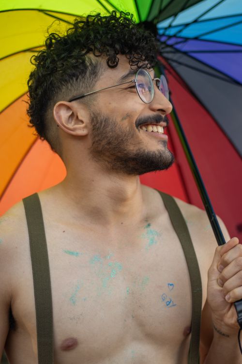 Free A joyful shirtless man smiles under a rainbow umbrella, celebrating diversity. Stock Photo