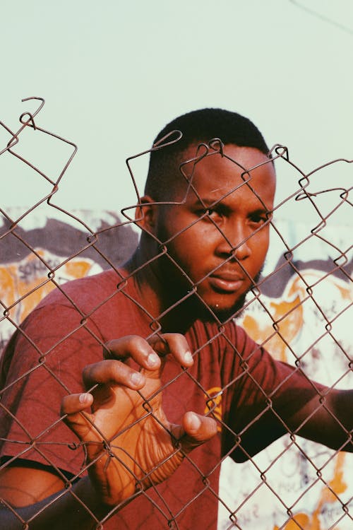 Young Man Standing behind a Chain Fence 