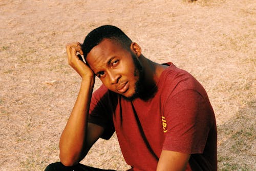 Young Man in Red T-Shirt Sitting on Ground