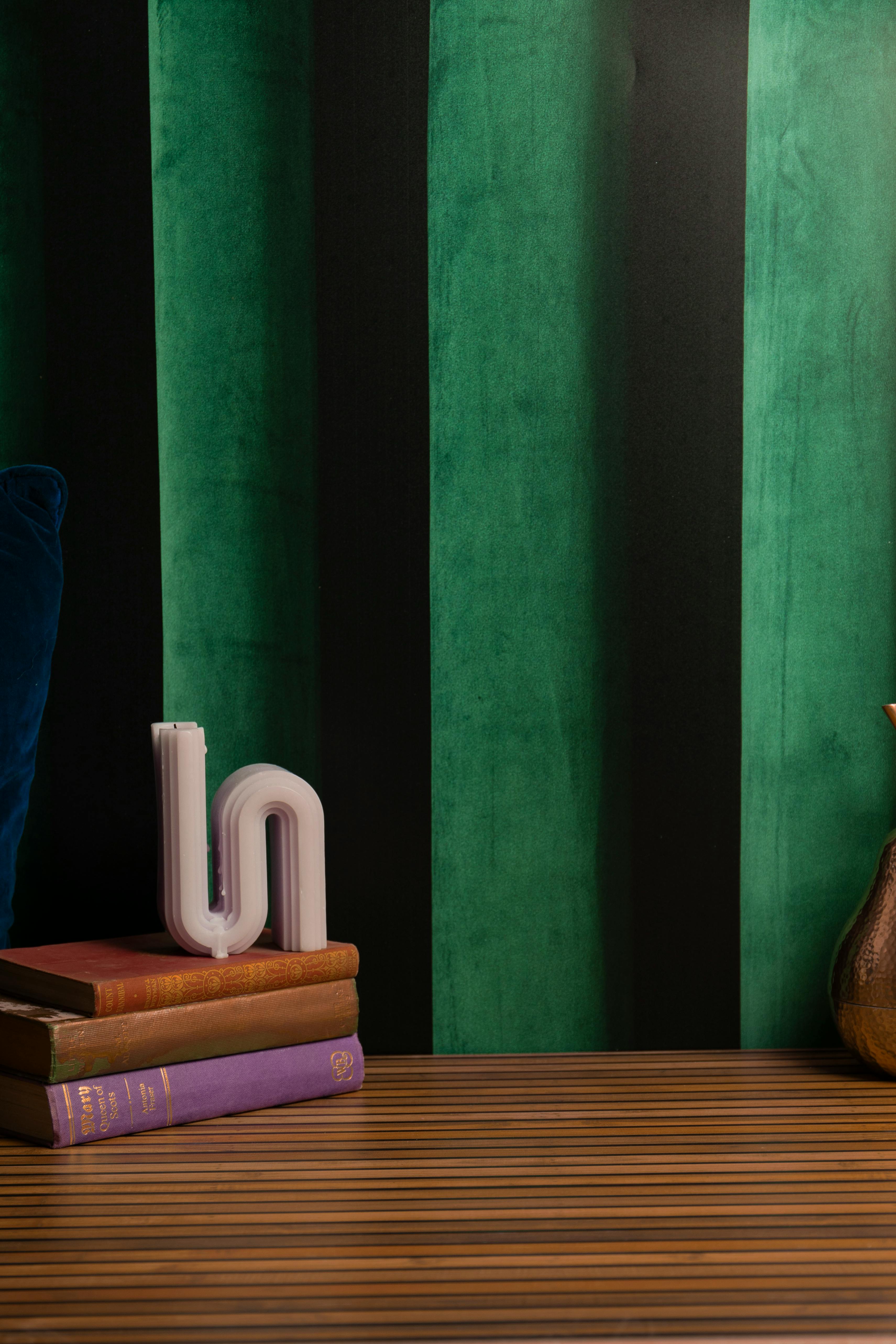 Stacked books with a uniquely shaped candle on a wooden table against a green and black wall.