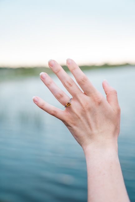 A hand with an engagement ring is raised against a serene water backdrop in Fort Lauderdale.