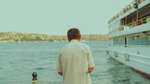 Man in Shirt Standing near Ferry on Sea Shore