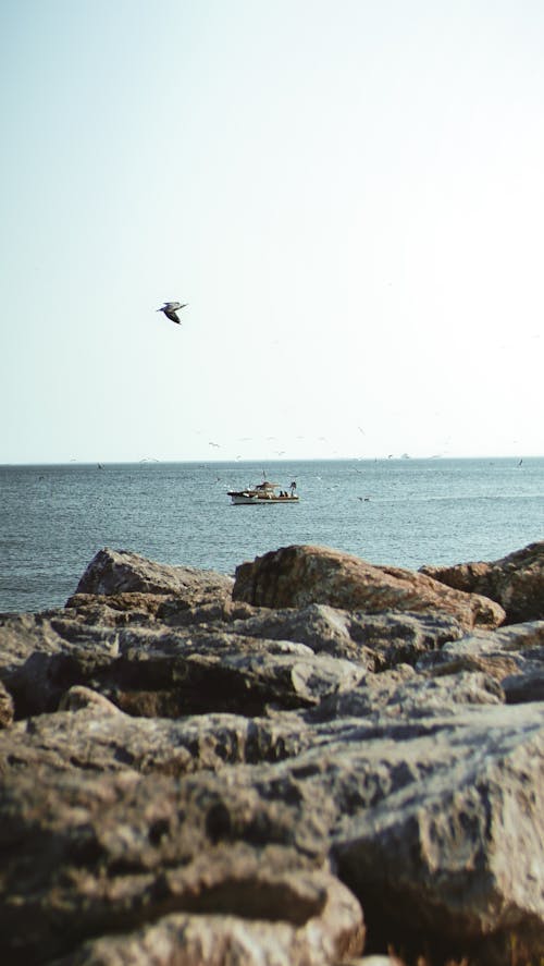 A Boat on the Sea Seen from a Rocky Shore 