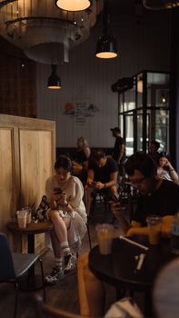 Adults sitting in a dimly lit cafe, engaged with their smartphones, creating a modern, urban ambiance.