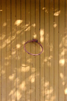 A rusty basketball hoop without a net on a vertical wooden wall with natural light shadows.