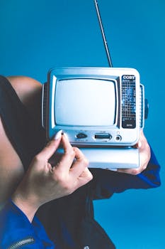 A woman holds a retro portable TV against a vibrant blue background, evoking nostalgia.