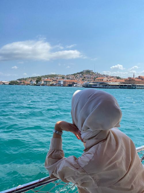 Free A woman in a hijab leans over a railing, admiring the beautiful coastal town view. Stock Photo
