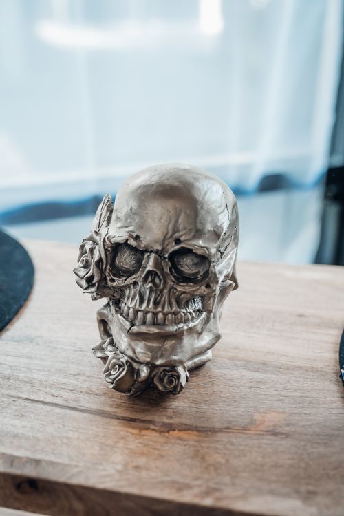 Free Close-up of a metal skull sculpture with rose decorations on a wooden surface. Stock Photo